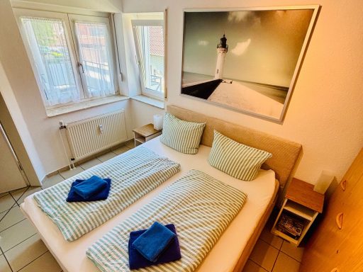 Helles Schlafzimmer mit Doppelbett, zwei Kissen und blauen Handtüchern auf der Bettdecke.