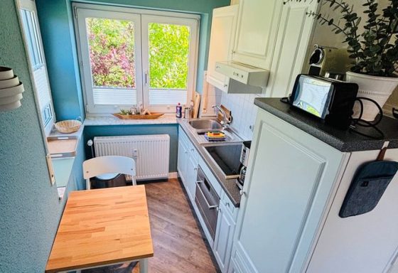 Kleine Küche mit blauen Wänden, weißer Einrichtung und einem Holztisch am Fenster.