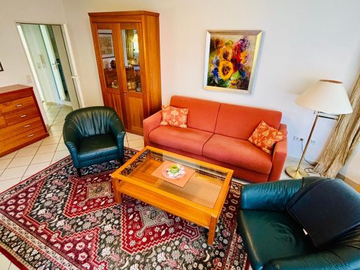 Gemütliches Wohnzimmer mit einem roten Sofa, zwei Sesseln und einem Holztisch auf einem Teppich.