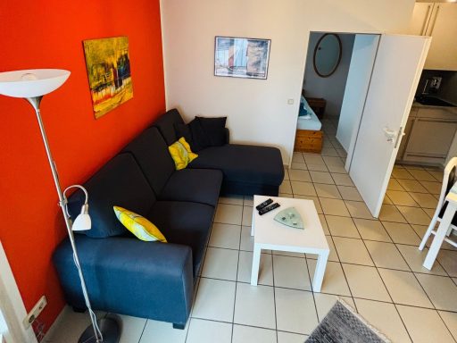Wohnzimmer mit einer dunkelblauen Couch, weißen Tisch und orangefarbener Wand.