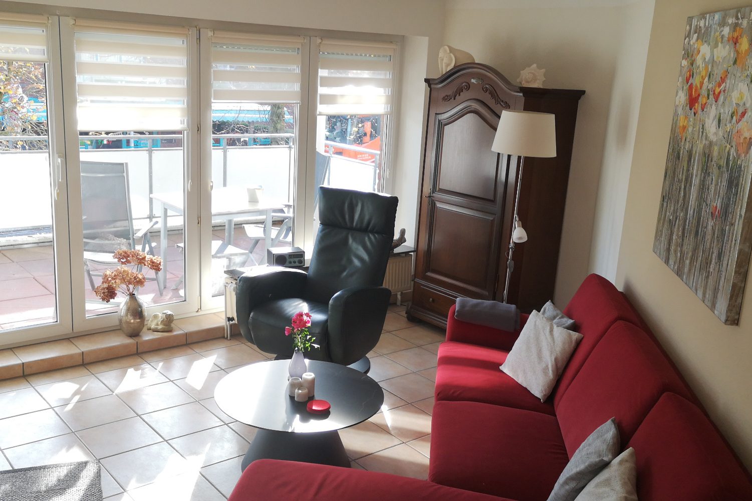 Helle Wohnsitzecke mit rotem Sofa, schwarzem Sessel und großem Fenster.