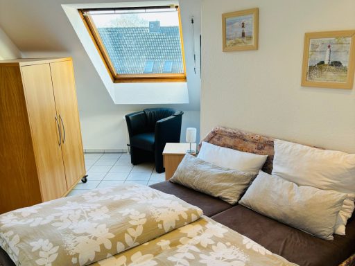 Gemütliches Schlafzimmer mit Doppelbett, Sesseln und Holzschrank unter dem Dachfenster.