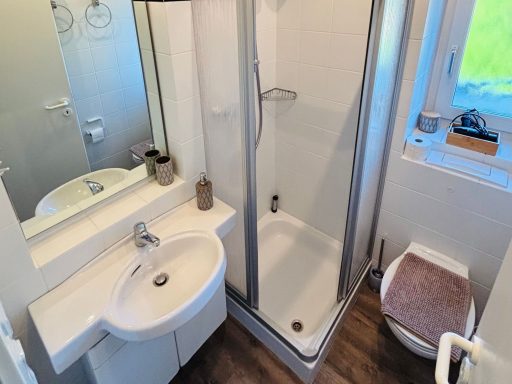 Helles Badezimmer mit Dusche, Waschbecken und Toilette sowie Fenster.