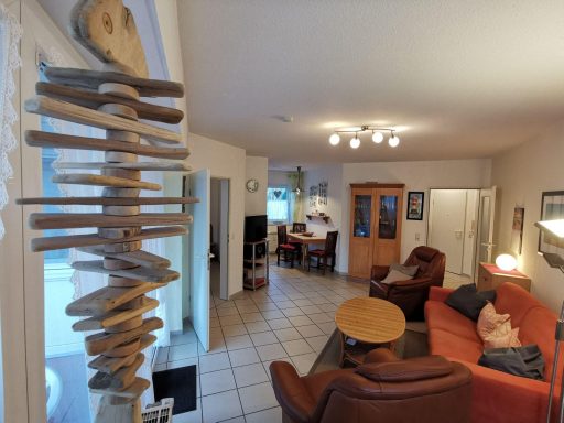 Gemütliches Wohnzimmer mit Sofa, Tisch und Fernseher, sowie einem dekorativen Holzobjekt.