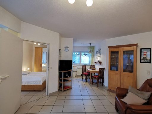 Helles Wohn- und Esszimmer mit einem Sofa, Tisch und angrenzendem Schlafzimmer.