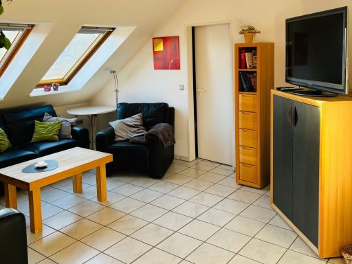 Helles Wohnzimmer mit schwarzen Sofas, Couchtisch und TV in einem Dachgeschoss.