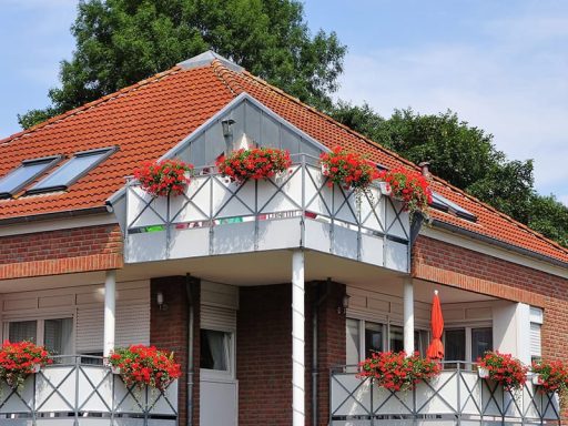 Haus mit rotem Dach und Balkon, geschmückt mit roten Blumen.