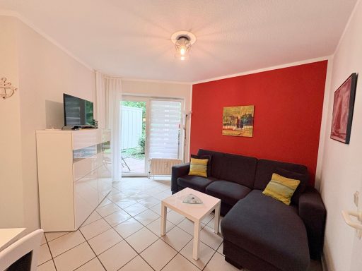 Wohnzimmer mit dunklem Sofa, Tisch, TV und roter Wandfarbe, Zugang zum Garten.