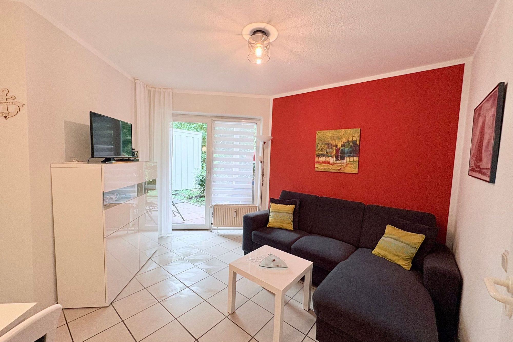 Wohnzimmer mit roter Wand, schwarzem Sofa, einem Tisch und einem offenen Küchenbereich.