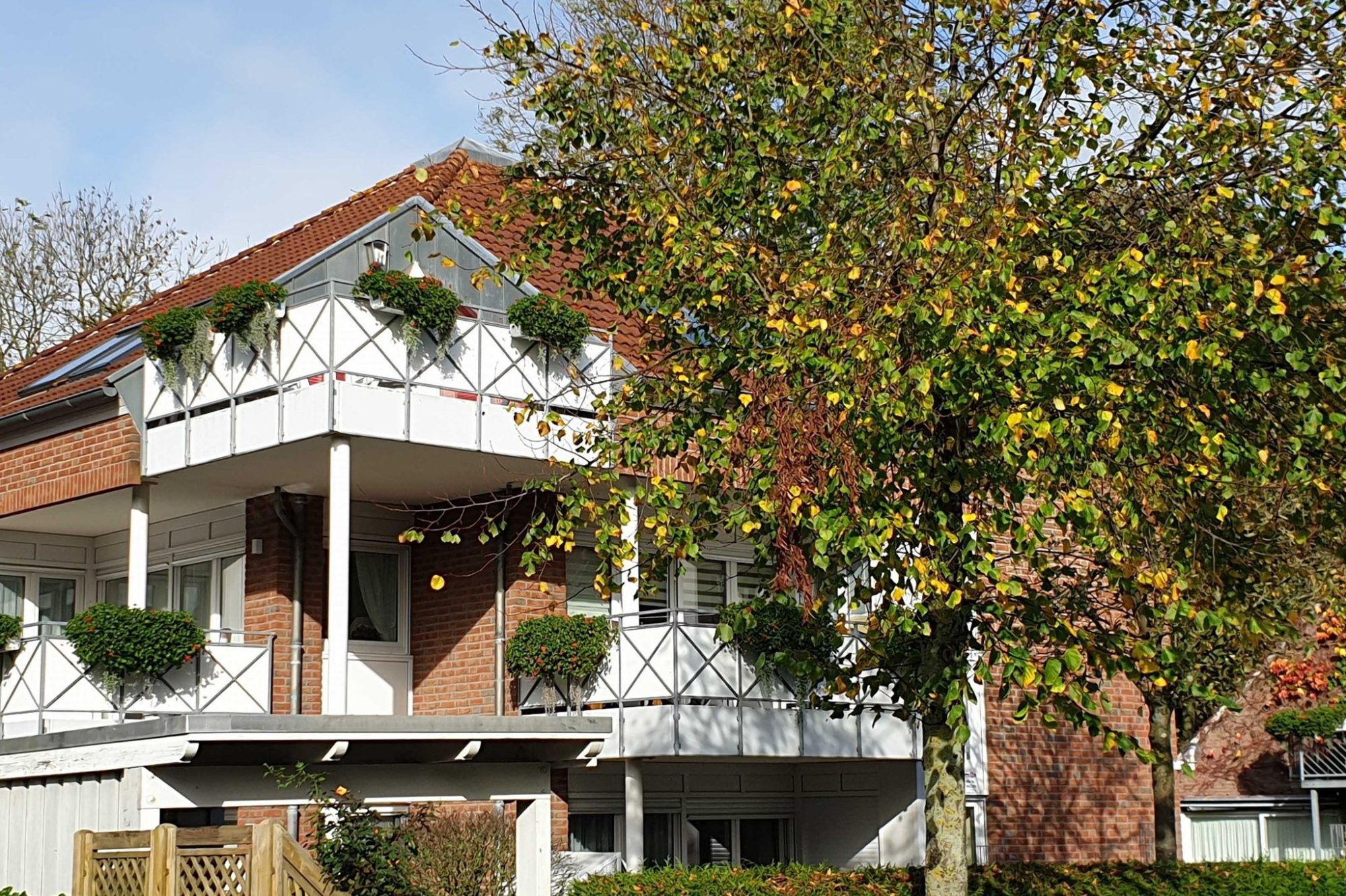 Zweifamilienhaus mit Balkon, umgeben von Bäumen und buntem Laub.