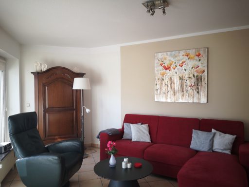 Gemütliches Wohnzimmer mit rotem Sofa, Sessel, Tisch und moderner Wandkunst.
