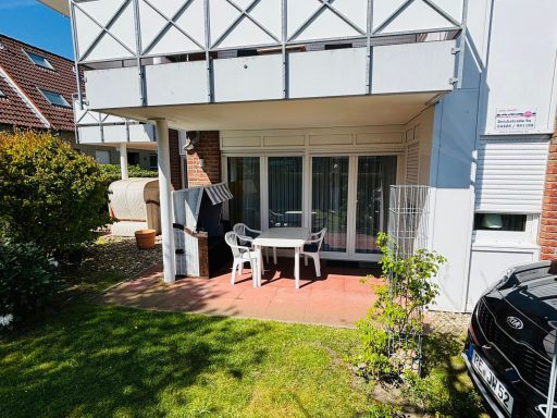 Terrasse mit Tisch und Stühlen, umgeben von Rasen und Pflanzen.