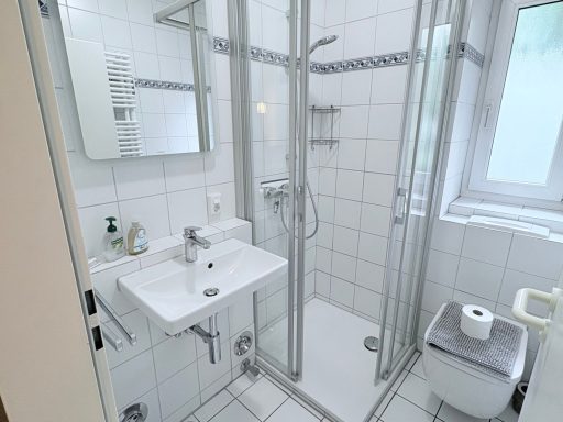 Modernes Badezimmer mit Dusche, Waschbecken und Toilette, helle Fliesen.