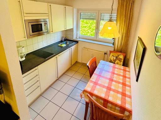 Kleine Küche mit Tisch, Stühlen, Fenster und einer Lampe, hell und einladend.