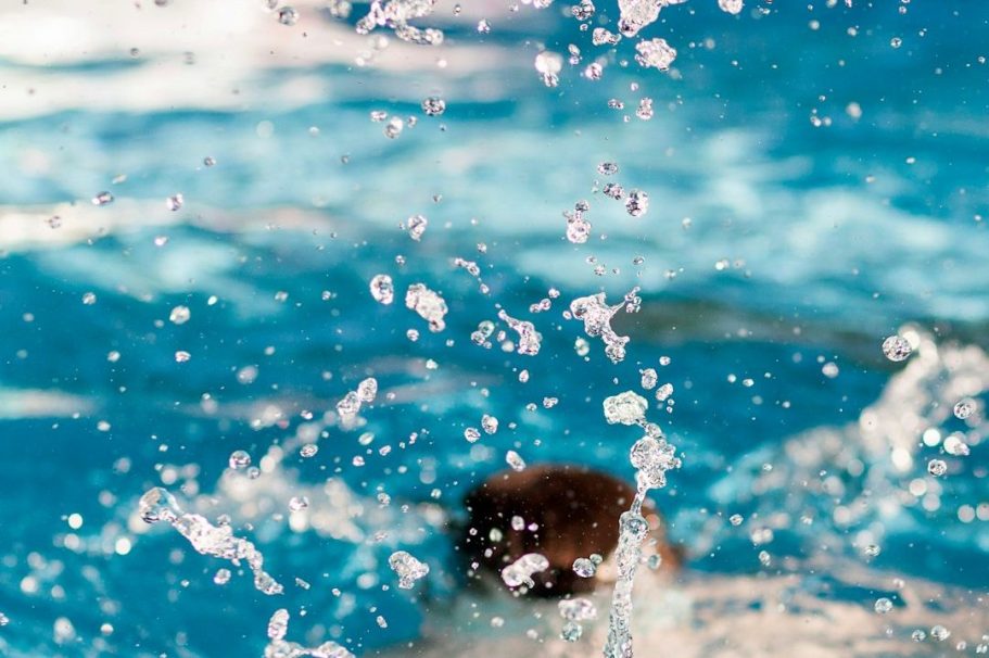 Spritzendes Wasser auf blauer Oberfläche, fokussiert auf einen schwimmenden Kopf.