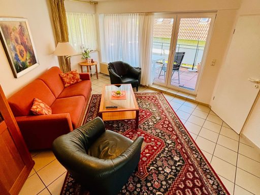 Gemütliches Wohnzimmer mit rotem Sofa, schwarzen Sesseln und einem Tisch auf einem Teppich.