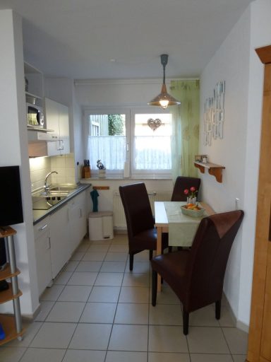 Kleine, moderne Küche mit Tisch, zwei Stühlen und Fensterlicht.