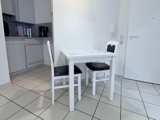 Kleine Küche mit einem weißen Tisch und zwei Stühlen, daneben Küchenschränke.