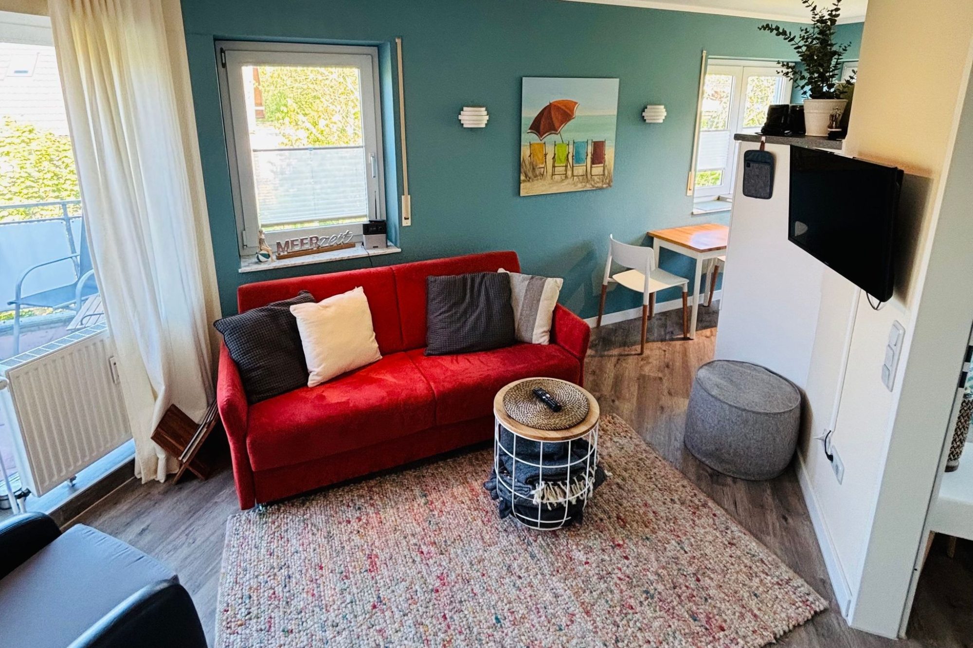 Heller Wohnbereich mit rotem Sofa, schwarzen Sessel und Zugang zur Terrasse.