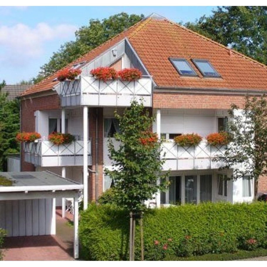 Drei Etagen Wohnhaus mit roten Blumenbalkonen und einem Garten.