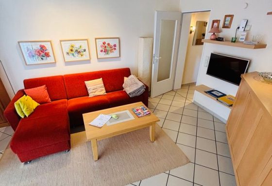 Gemütliches Wohnzimmer mit rotem Sofa, Holztisch und Bildern an der Wand.