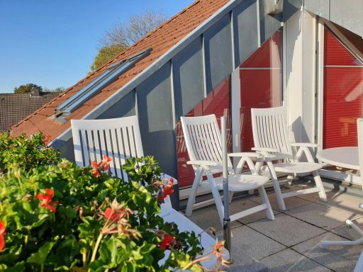 Blauer Himmel, Balkon mit weißen Stühlen und blühenden Pflanzen.